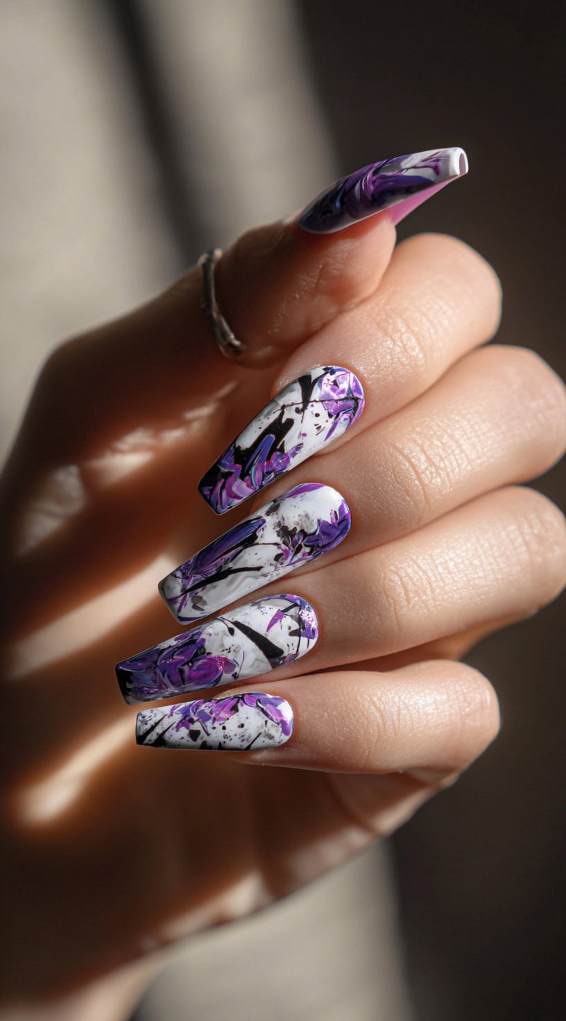 Long coffin-shaped nails painted with a chaotic swirl of purple, black, and white splashes, resembling comic book graffiti.