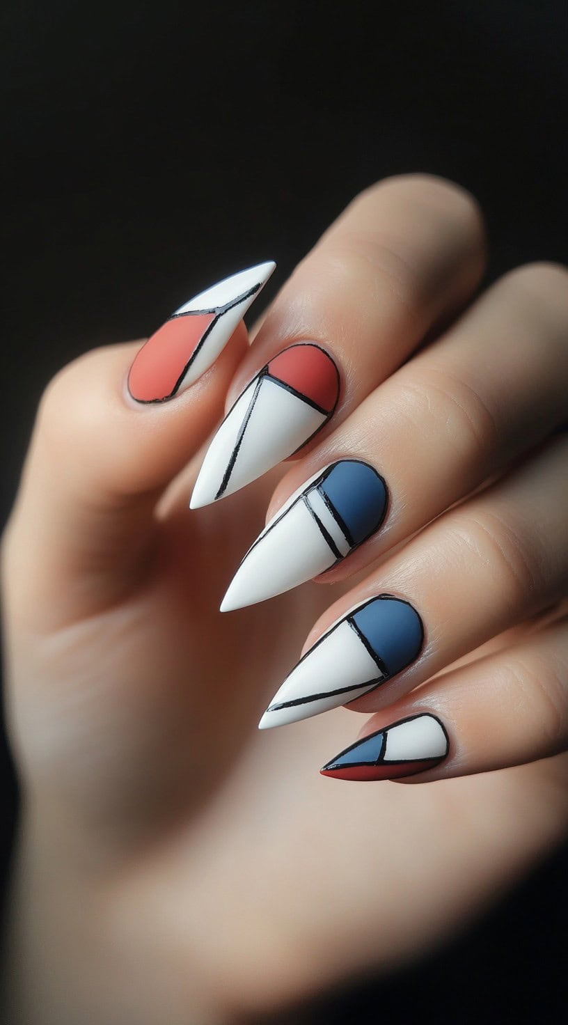 A hand with sharp stiletto nails featuring an abstract design with red, blue, and white geometric sections outlined in black.