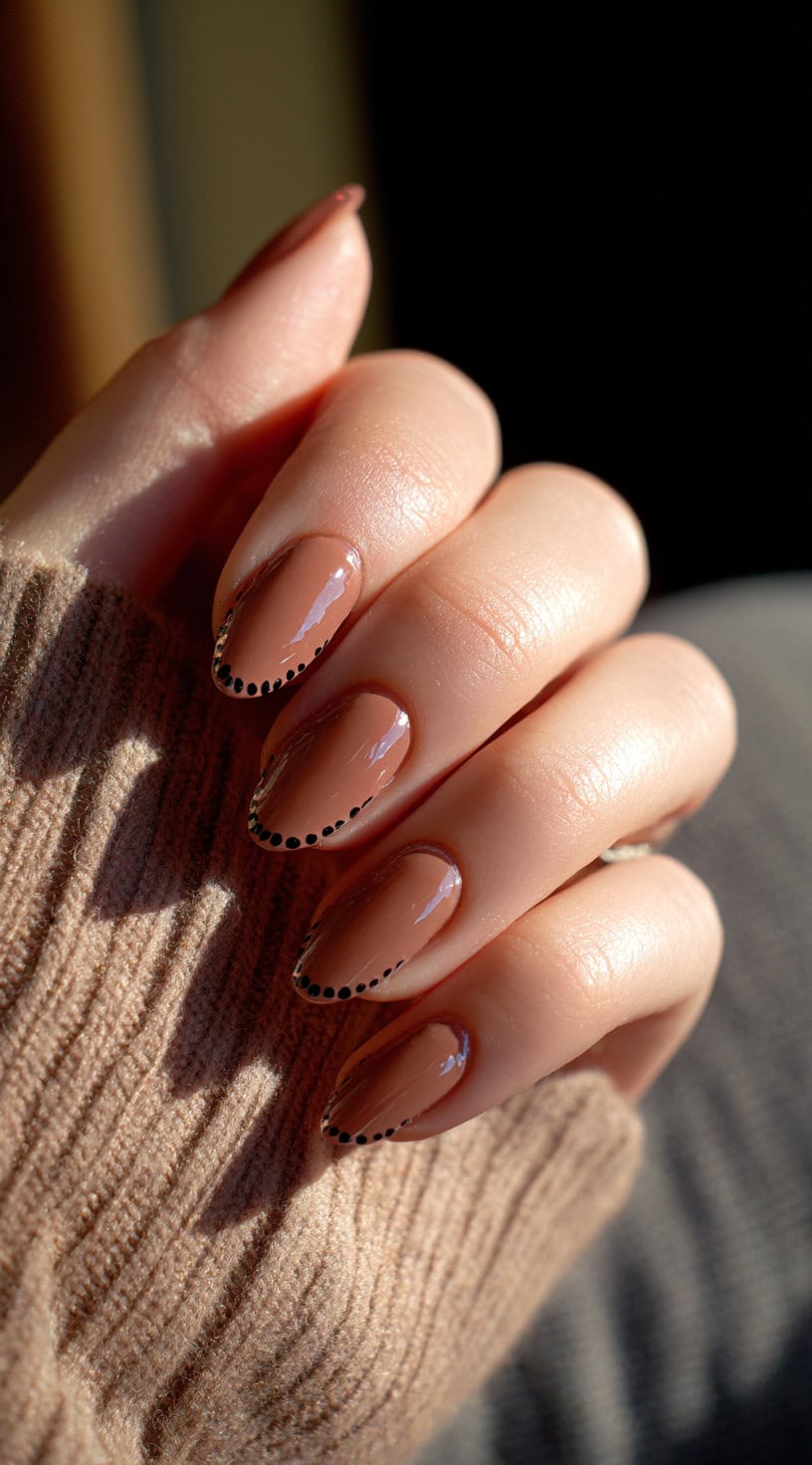 Almond nails painted in a warm chocolate nude with fine black dotted detailing along the tips.