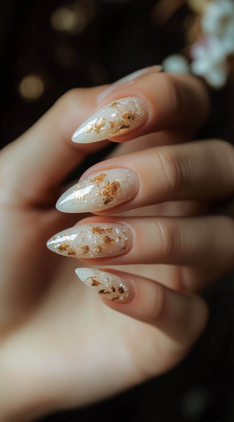 Five almond-shaped nails with a translucent cream base and scattered gold foil flakes.