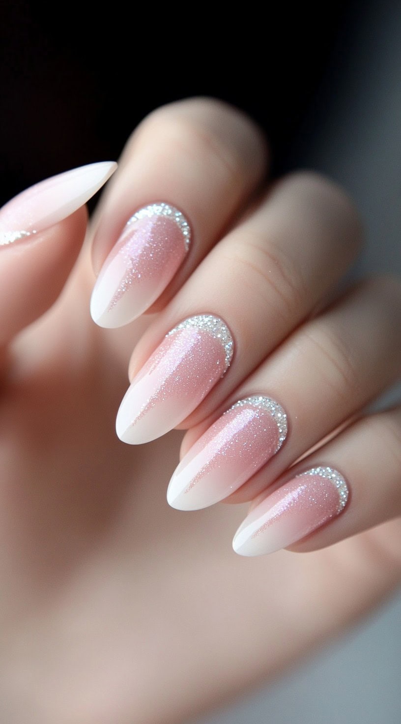 Almond-shaped nails with a pink-to-white ombre and fine silver glitter detailing at the cuticle area.