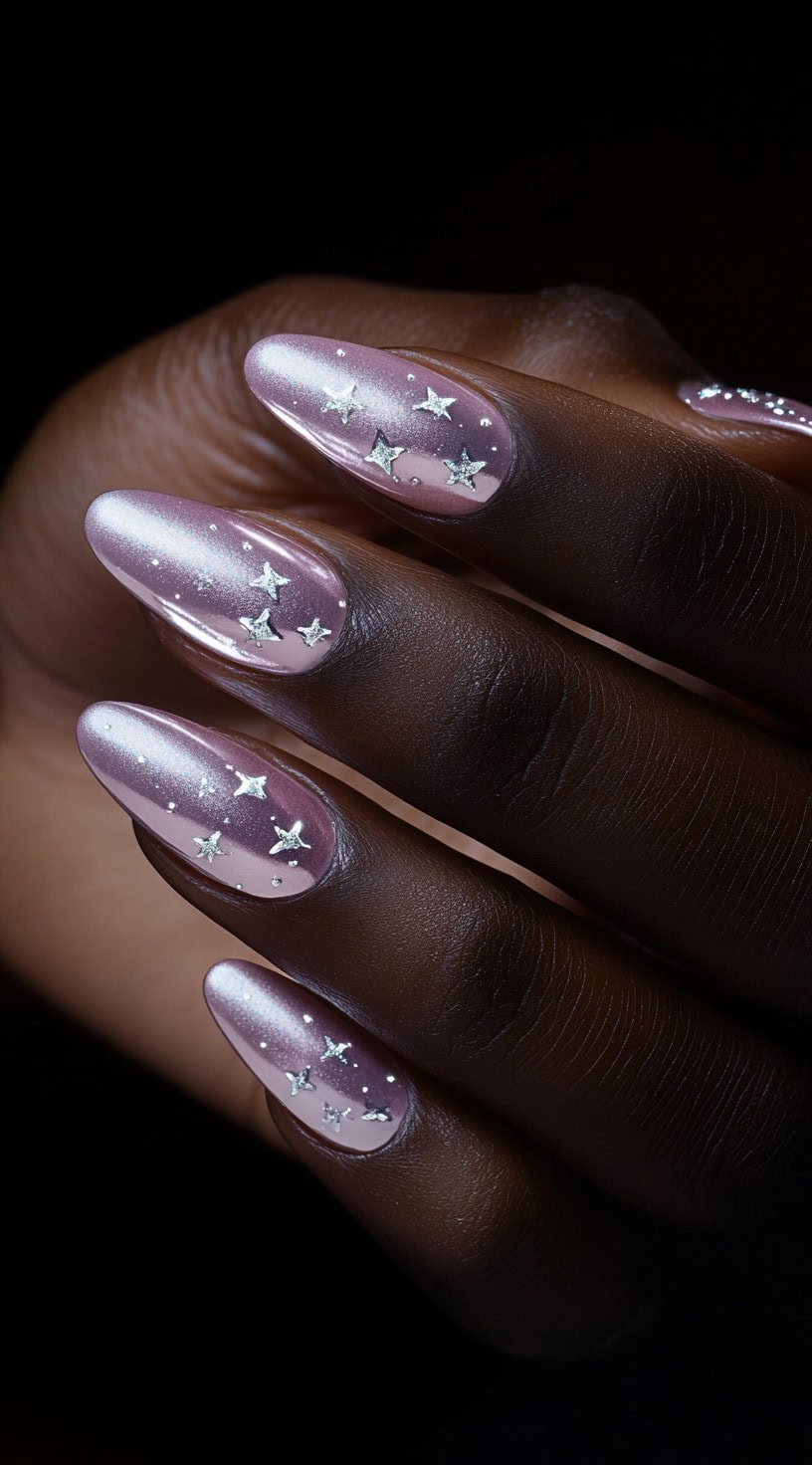 Almond-shaped light pink chrome nails decorated with silver star-shaped decals.