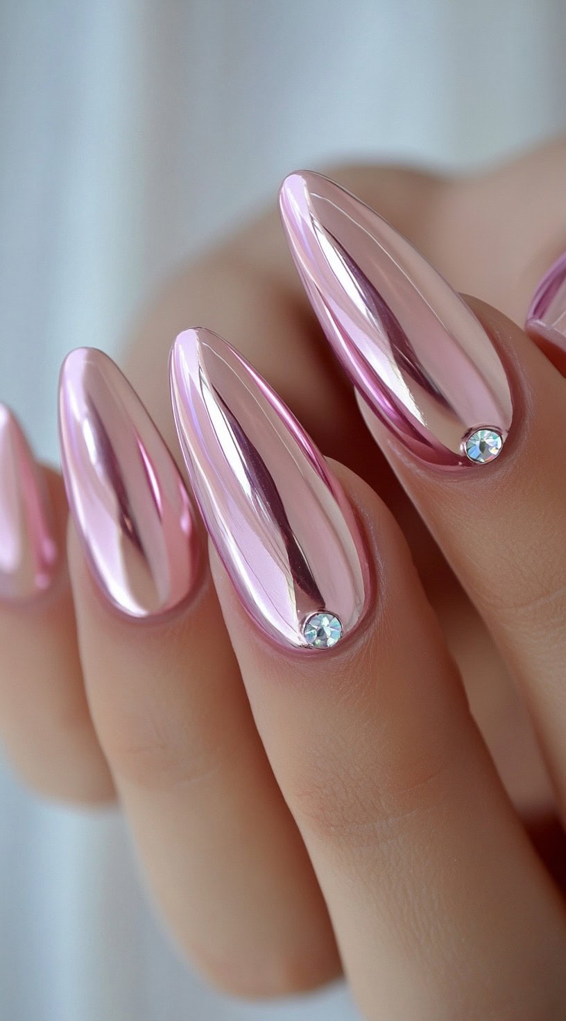 Almond-shaped light pink chrome nails with a single round rhinestone placed near each cuticle.