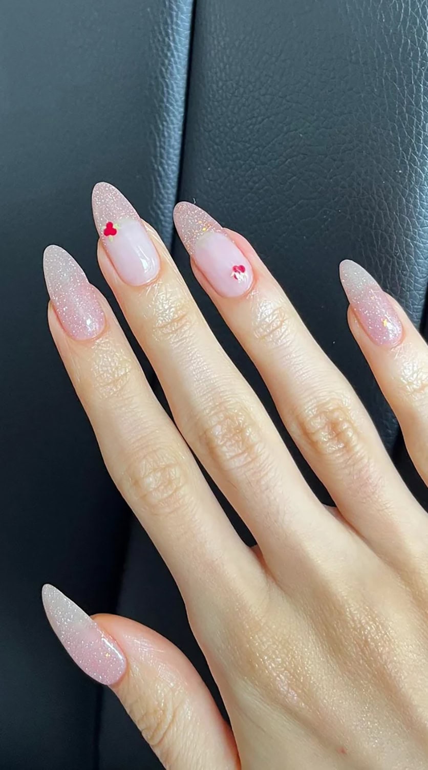 Long fingers featuring sparkly almond-shaped nails with tiny red heart nail art.