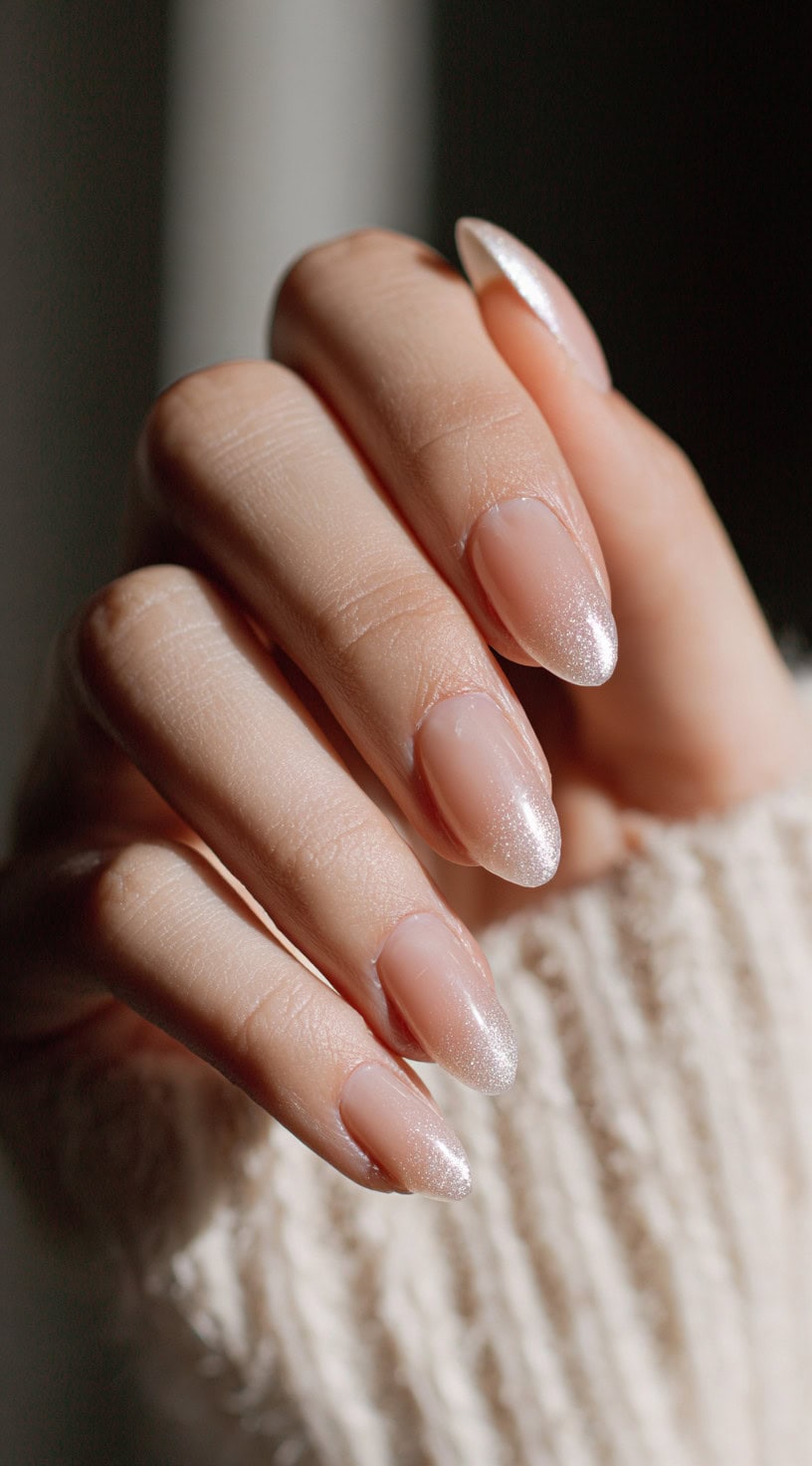 Almond-shaped nails with a translucent nude base and subtle silver glitter ombre tips.