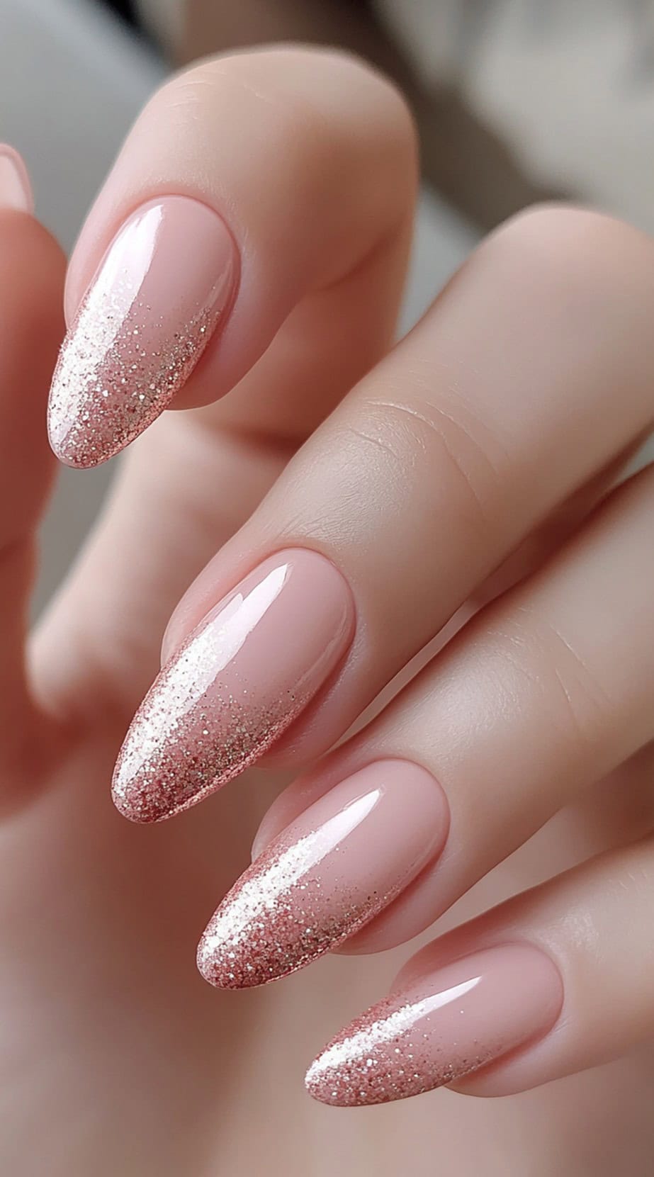 A set of almond-shaped nails with a soft pink base fading into glittery rose gold tips.