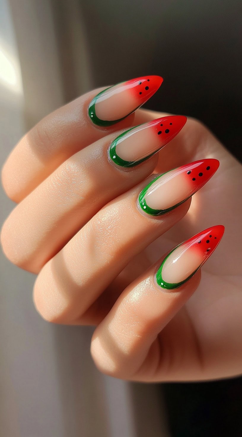 Almond-shaped nails with a gradient watermelon design in red and green, featuring tiny black seed dots.