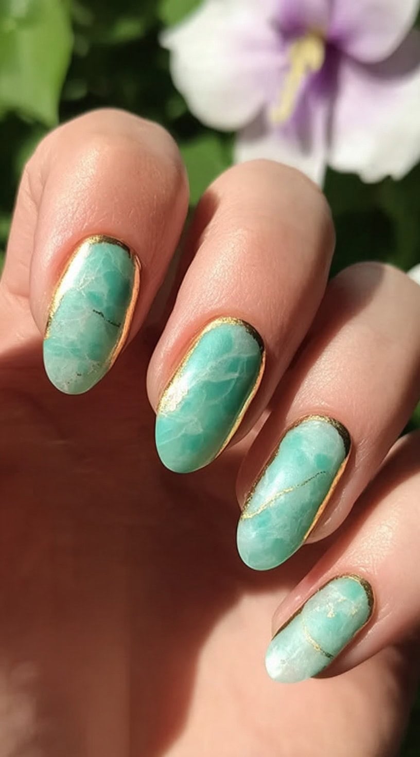 Oval nails painted in soft amazonite jade and framed by a clean metallic gold outline along every cuticle.