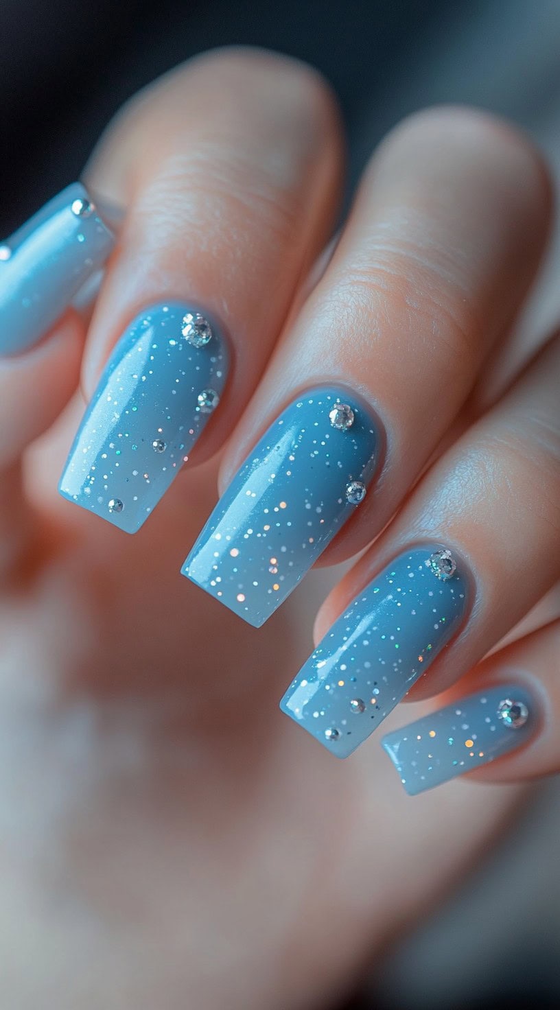 Soft baby blue ombre nails with fine glitter and subtle crystal embellishments.