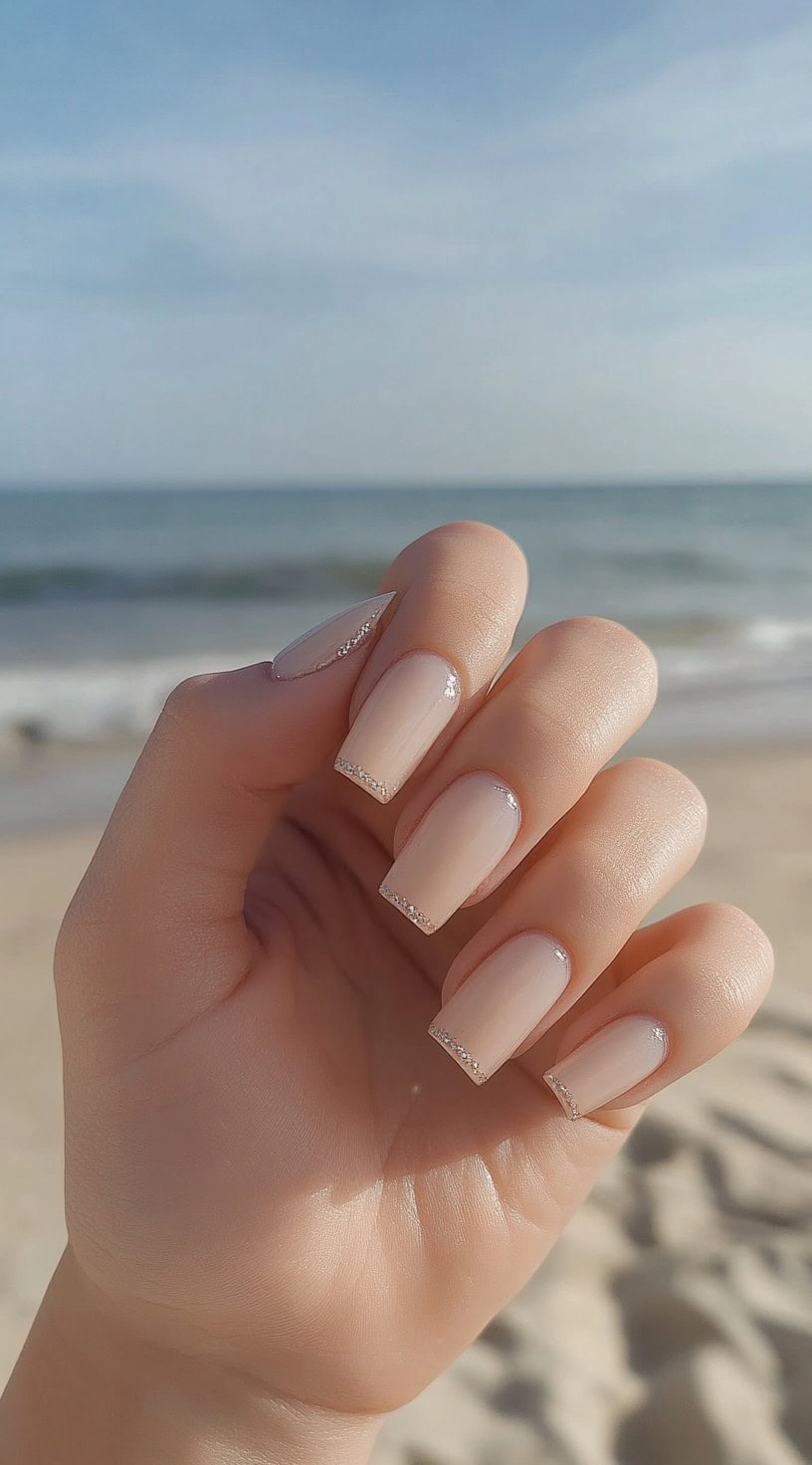 Hand with square-shaped nude nails featuring subtle pearl tips.