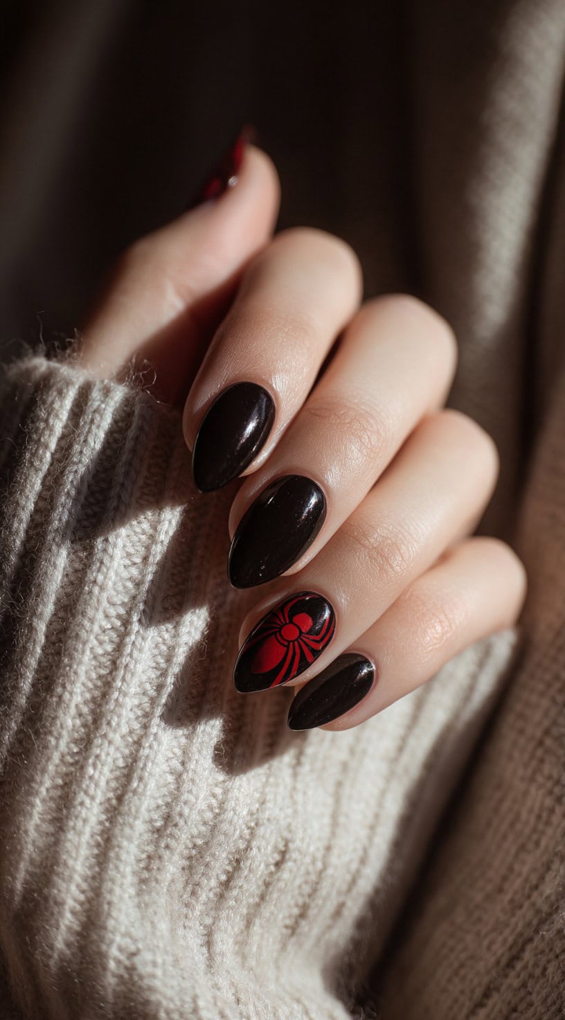 A hand with short almond-shaped black nails and a red spider accent on the ring finger.