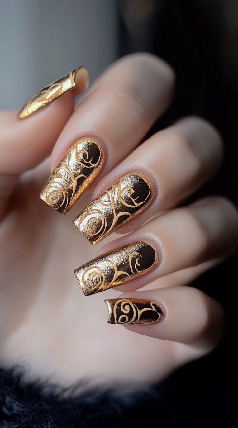 A hand with long, square-shaped nails featuring a gold base with intricate embossed swirl patterns in a deeper metallic shade.