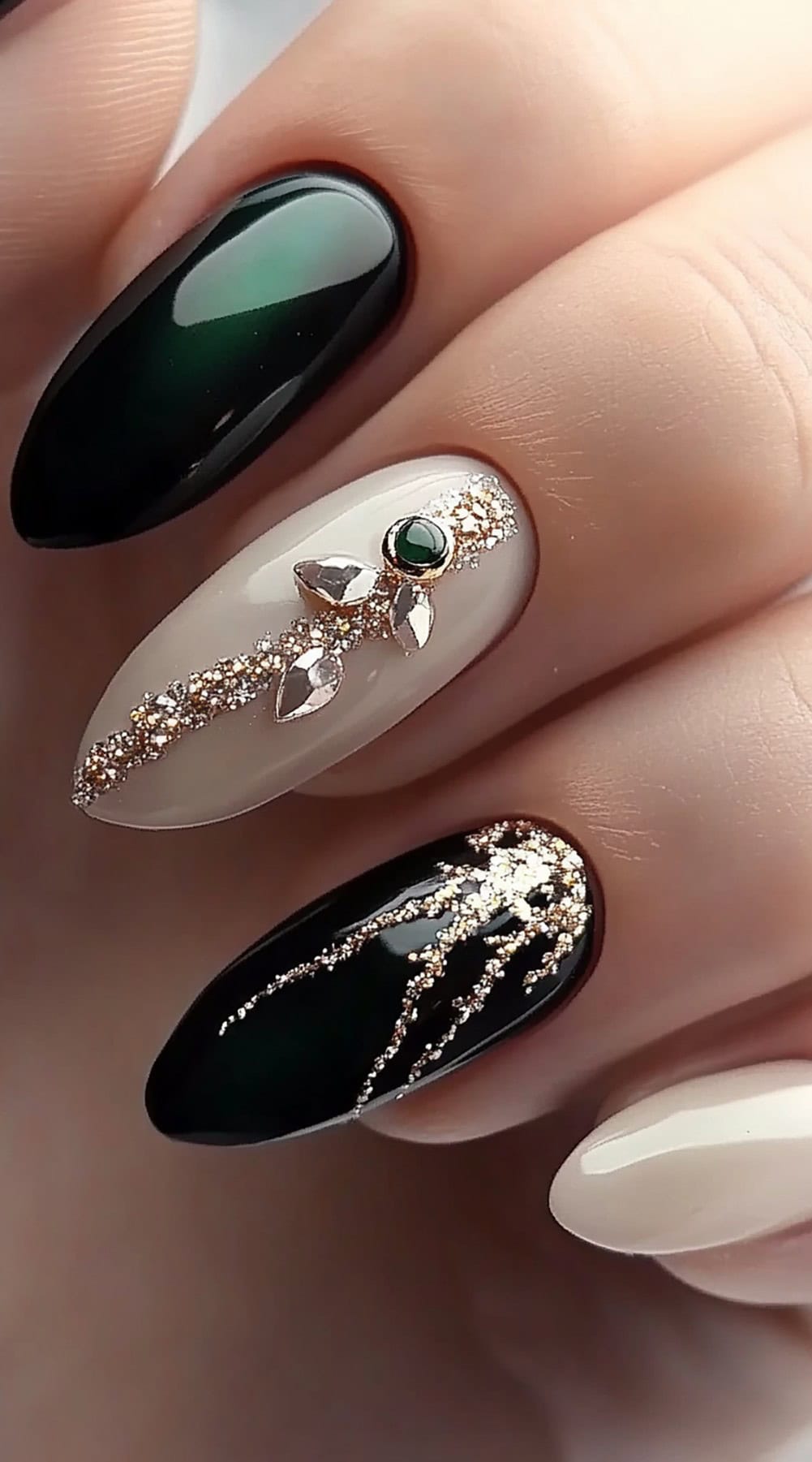 A set of almond-shaped nails featuring a deep green-to-black ombre effect, gold glitter detailing, and elegant gem embellishments.