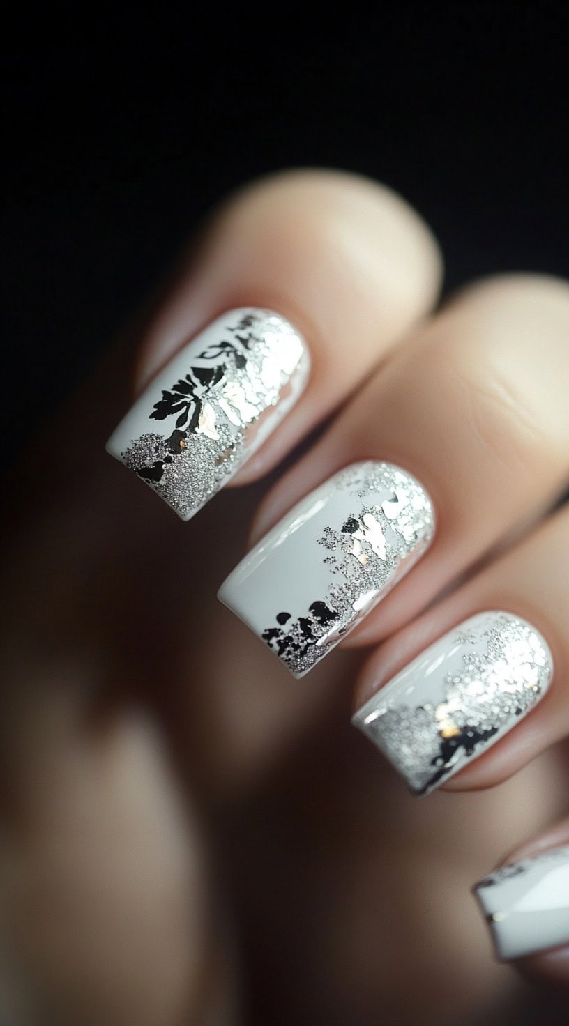 A set of square-shaped wedding nails with a white base, decorated with silver foil and black floral designs along the tips.