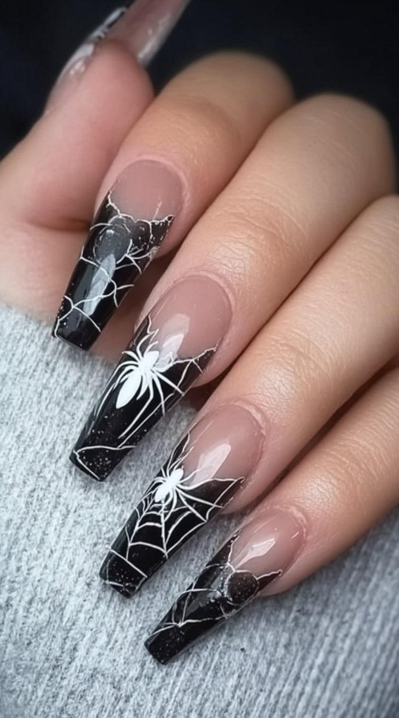 A hand with long black coffin-shaped nails that feature nude bases and angled white spiderweb French tips with white spider decals.
