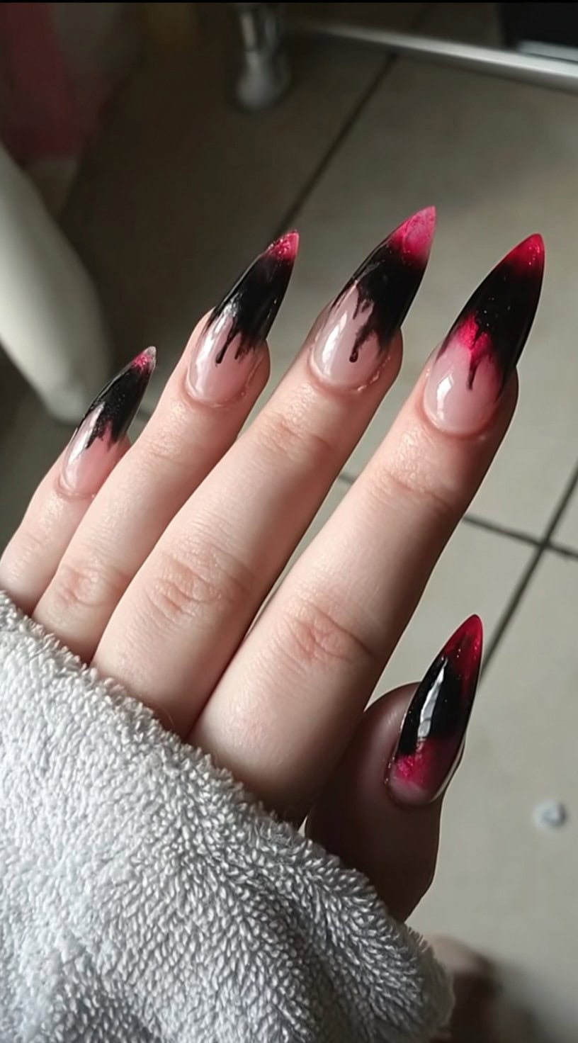 Long almond nails featuring sheer pink bases with dripping black and red flame-like tips.