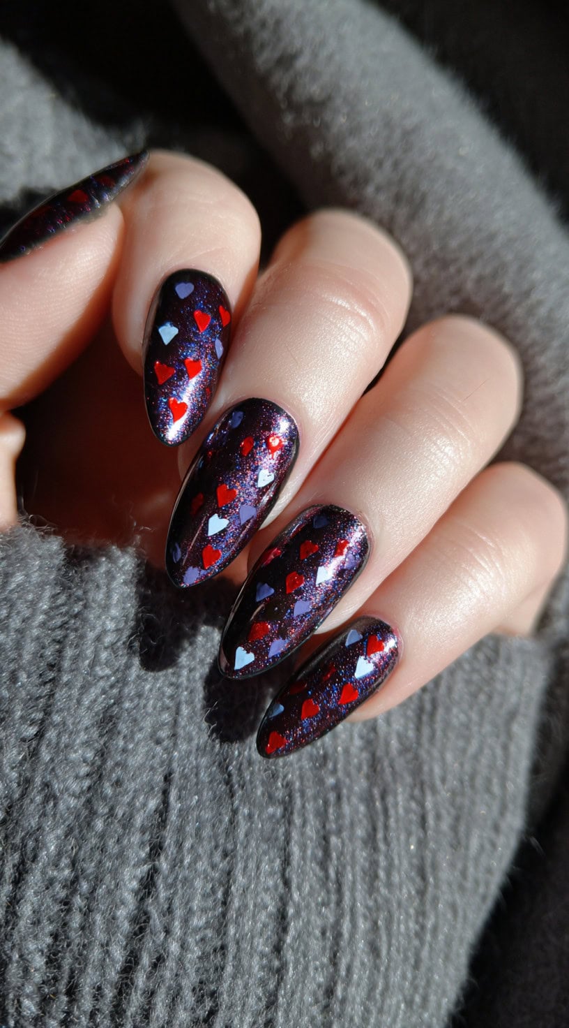 Almond-shaped nails with a dark glittery base and layered red and white heart shapes scattered across all fingers.