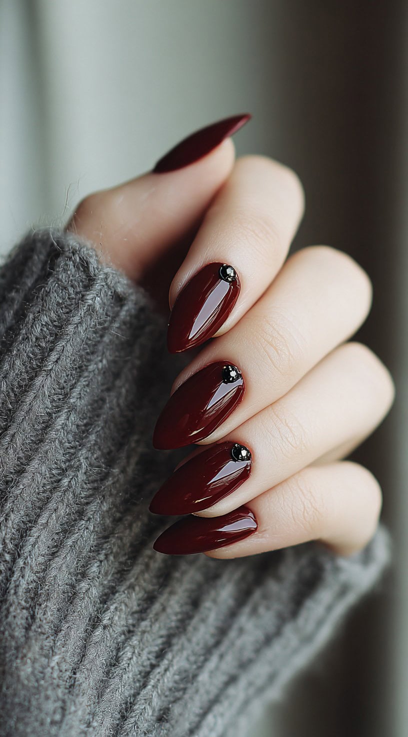 Almond-shaped nails painted a glossy blood-red with black rhinestone studs near the cuticles.