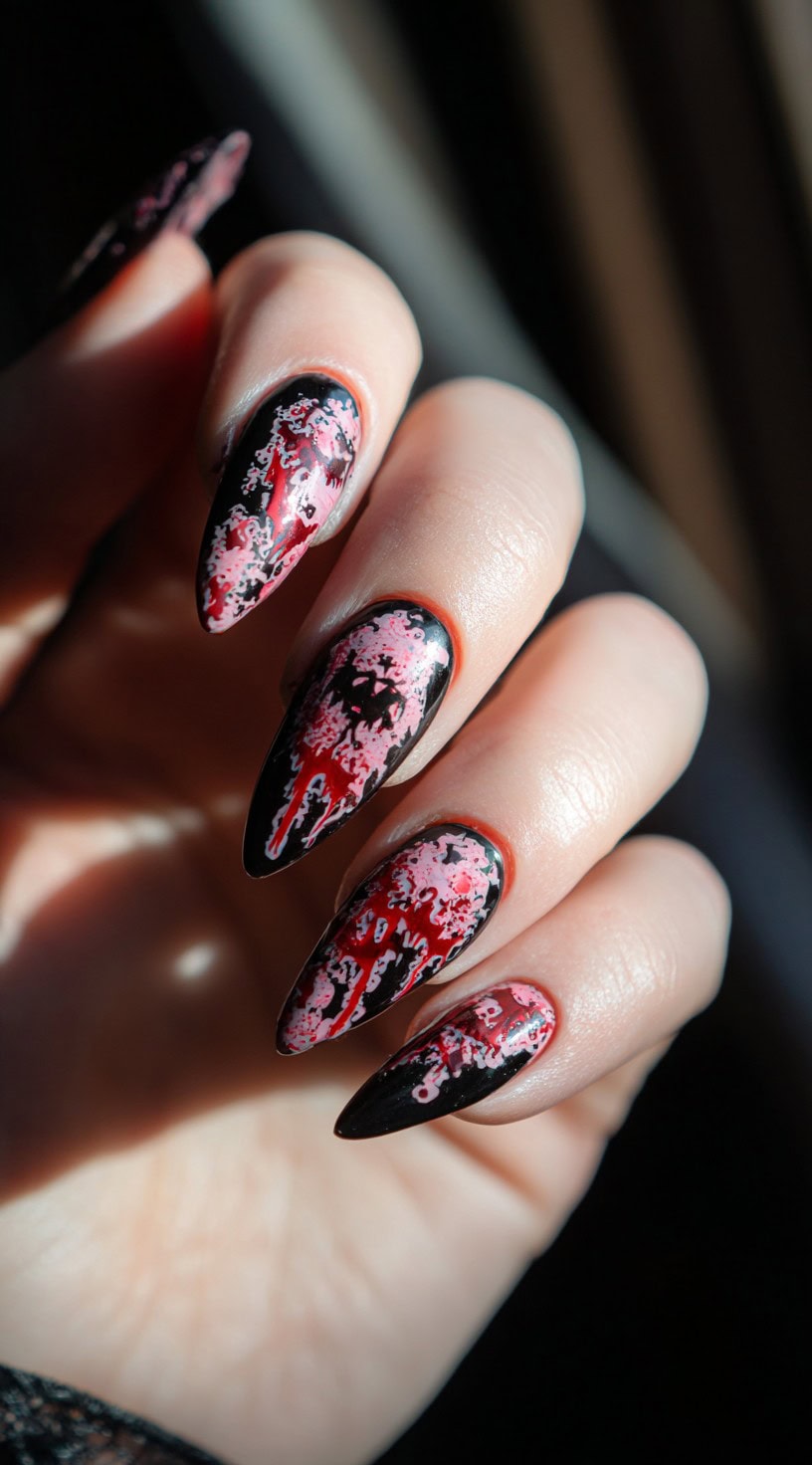 A hand with almond-shaped nails featuring red, black, and pink blood-drip style splatter in a grungy horror design.