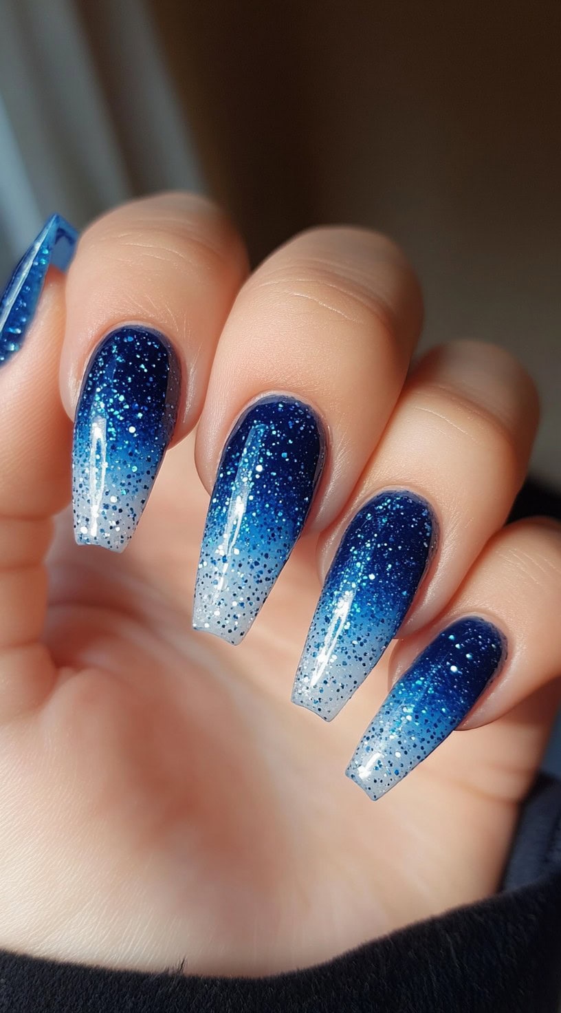 Long coffin-shaped nails featuring a gradient from deep blue to white with fine glitter accents.