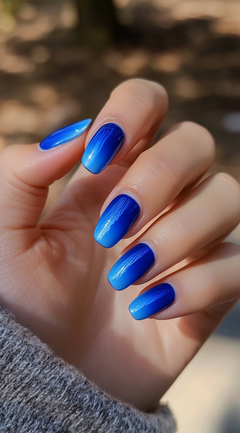 Ombre almond-shaped nails transitioning from deep blue to a soft, sky-blue tip.