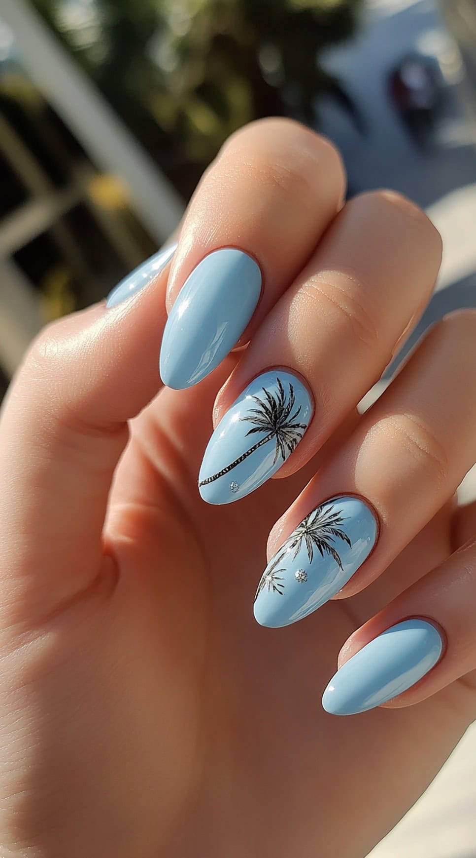 Hand with almond-shaped blue nails featuring black palm tree silhouettes.