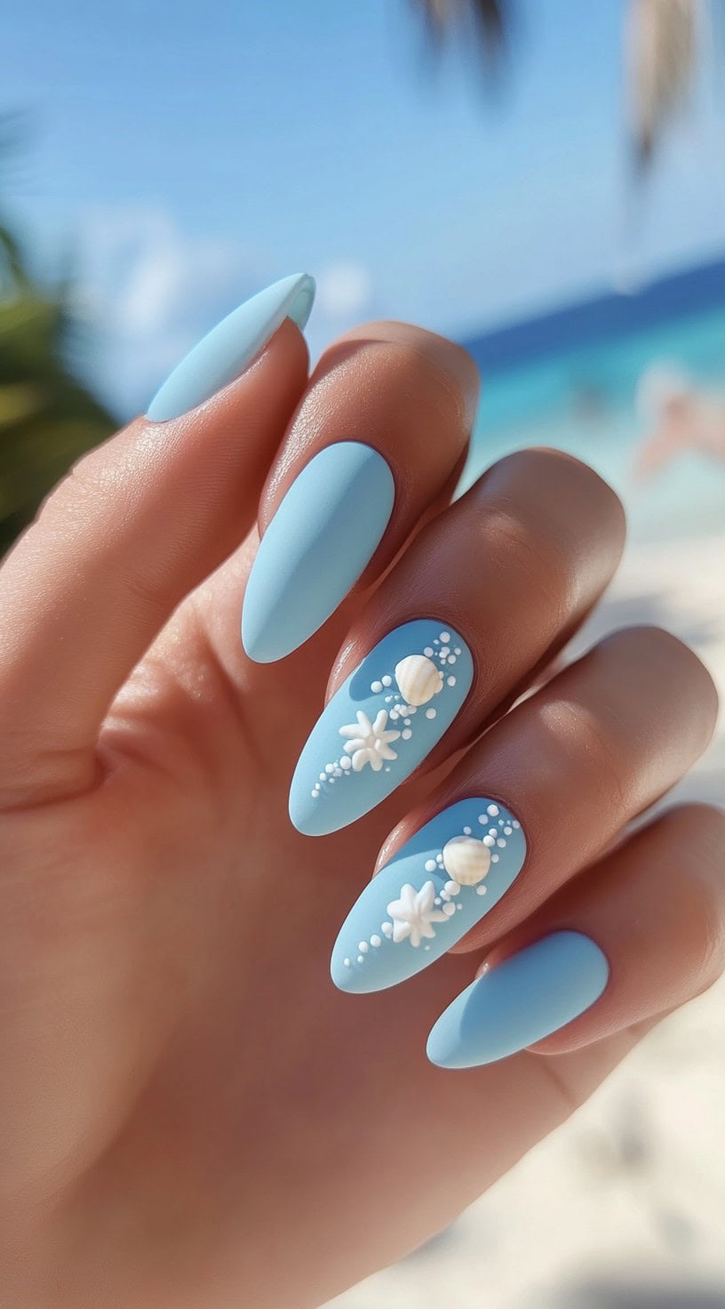 Hand with almond-shaped blue nails featuring white seashell and starfish accents.