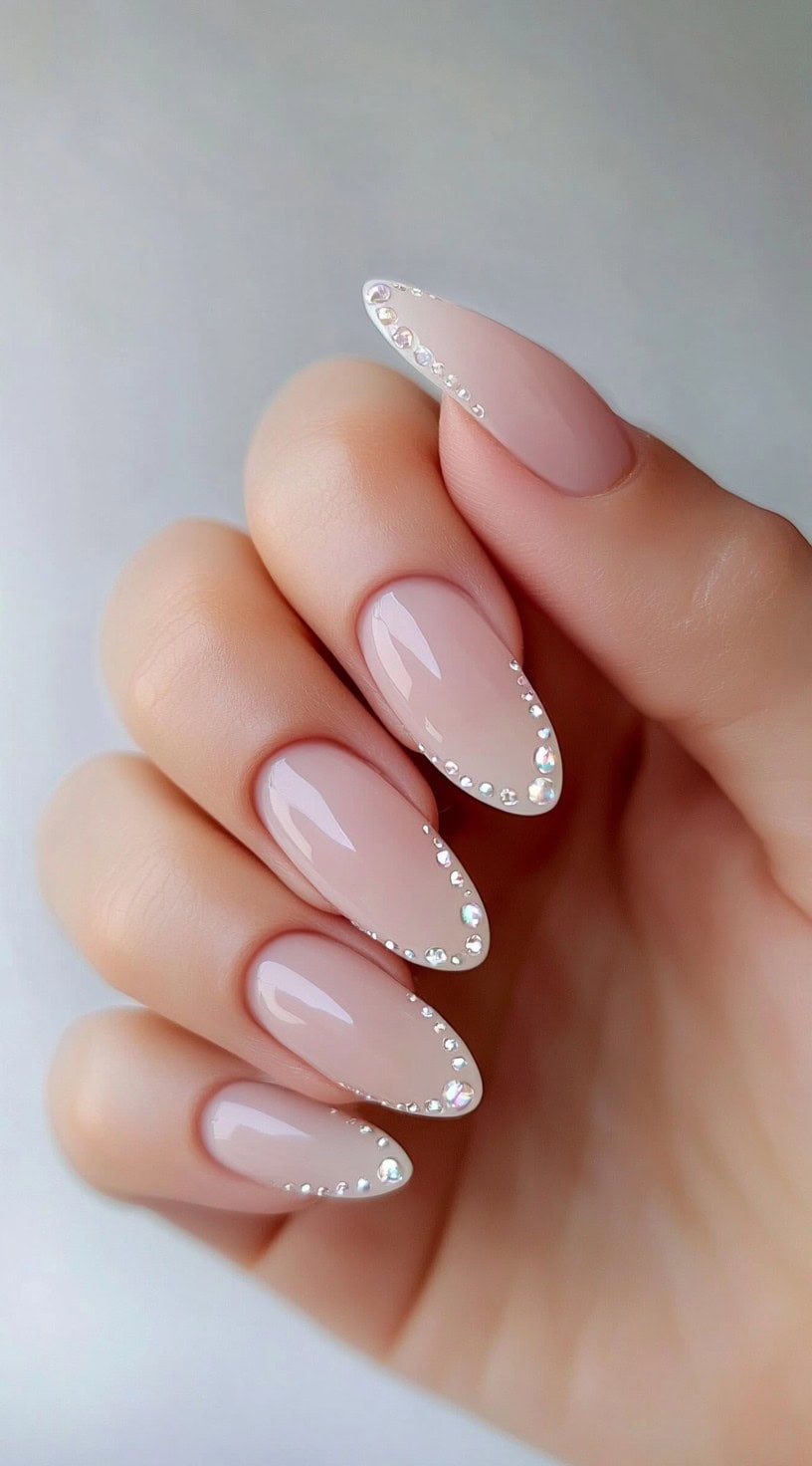 Glossy almond nails in blush pink with miniature crystals tracing the edges.