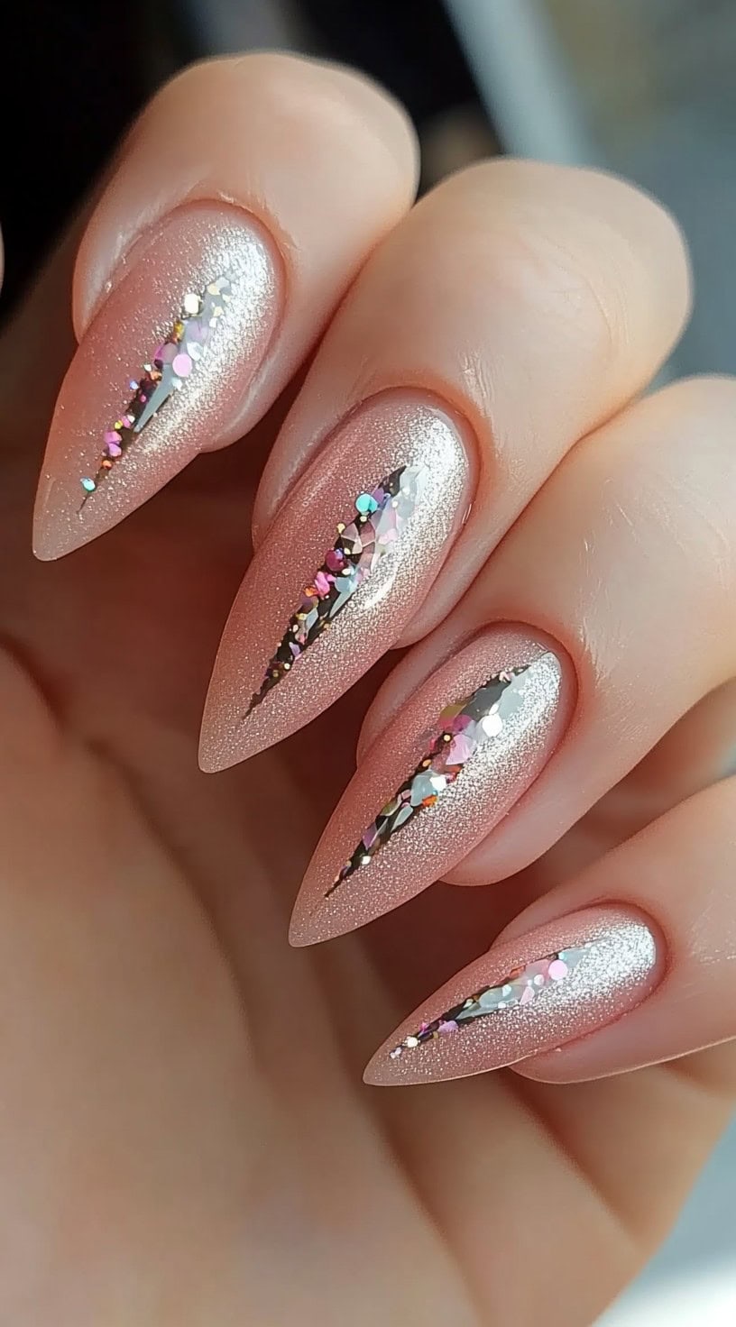 Almond-shaped nails in a soft blush tone with a metallic silver shimmer and an angular glitter cut-crease design in the center.