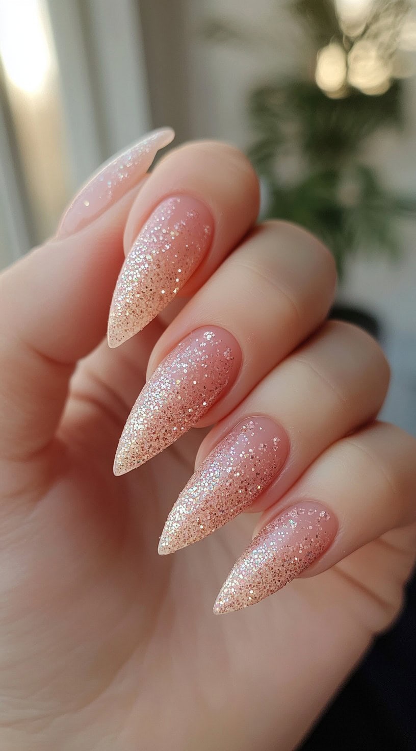 Elegant stiletto-shaped nails featuring a soft nude-pink base with a cascading gradient of fine blush gold glitter.