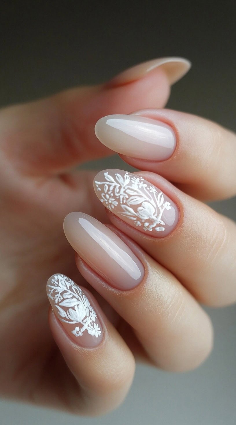 Five oval-shaped nails with a blush nude base, featuring intricate white floral lace detailing on two accent nails.
