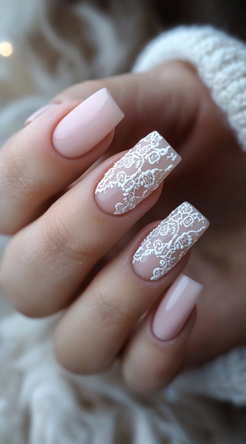 Soft blush square nails featuring intricate white lace detailing over two accent nails.