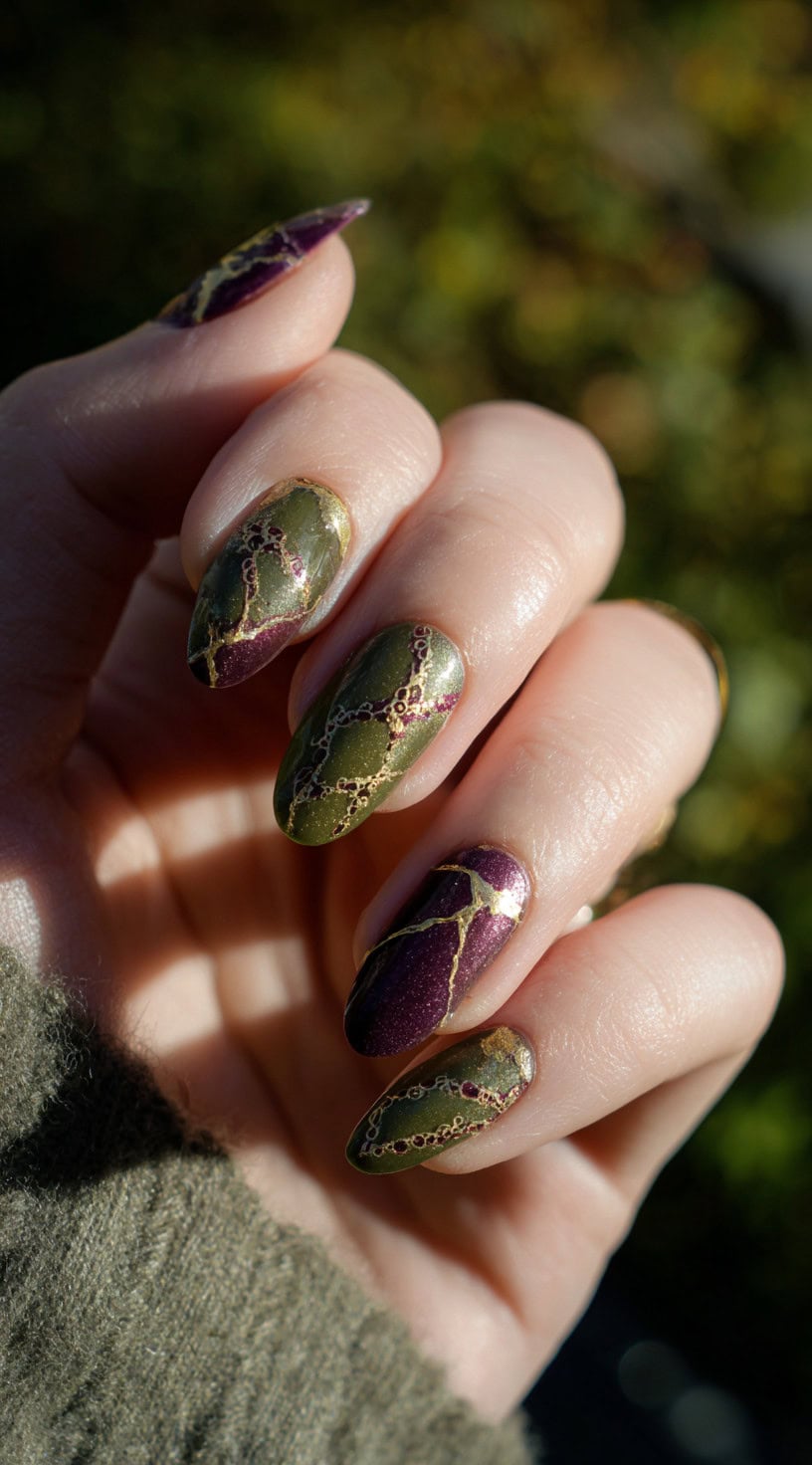 Almond-shaped nails with dark olive and deep purple polish, crossed with gold vein patterns resembling a spellbook cover.
