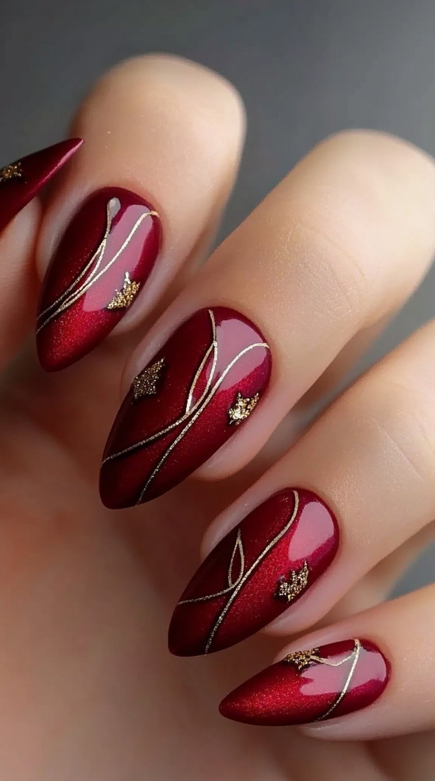 Almond-shaped nails in a rich burgundy hue, adorned with fine gold lines and tiny gold star embellishments.