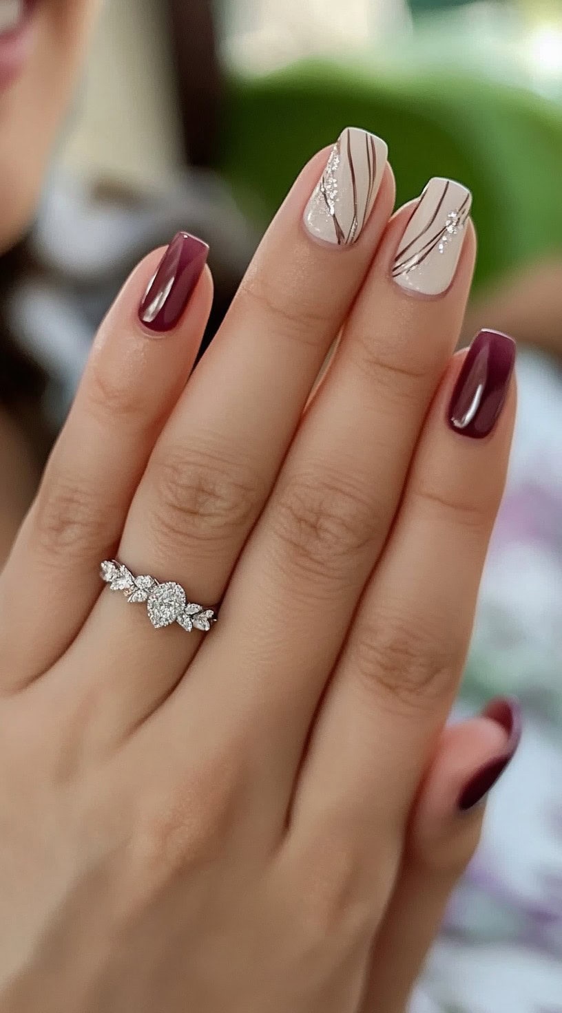 Five square nails alternating between glossy burgundy and creamy white, with the lighter nails featuring fine metallic stripes and scattered sparkle.