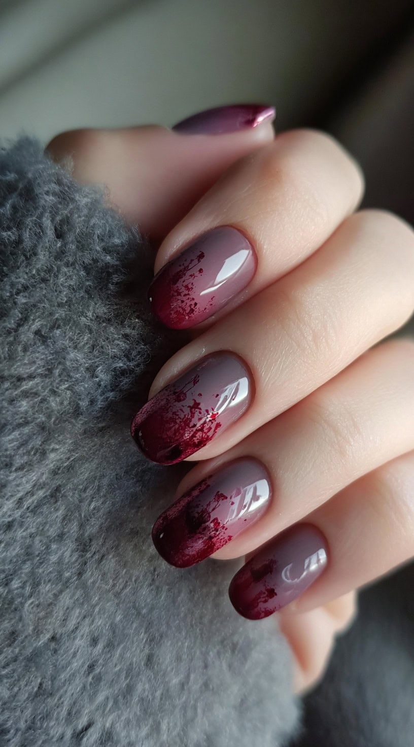 A hand with short round nails fading from taupe to deep burgundy with abstract splatter details.