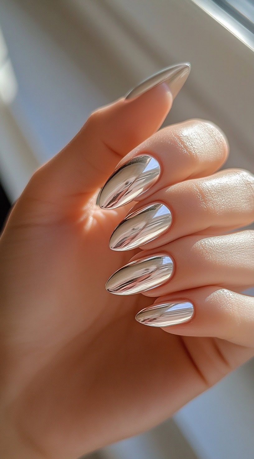 Five almond-shaped nails painted with a pure silver chrome finish that reflects light like a mirror.