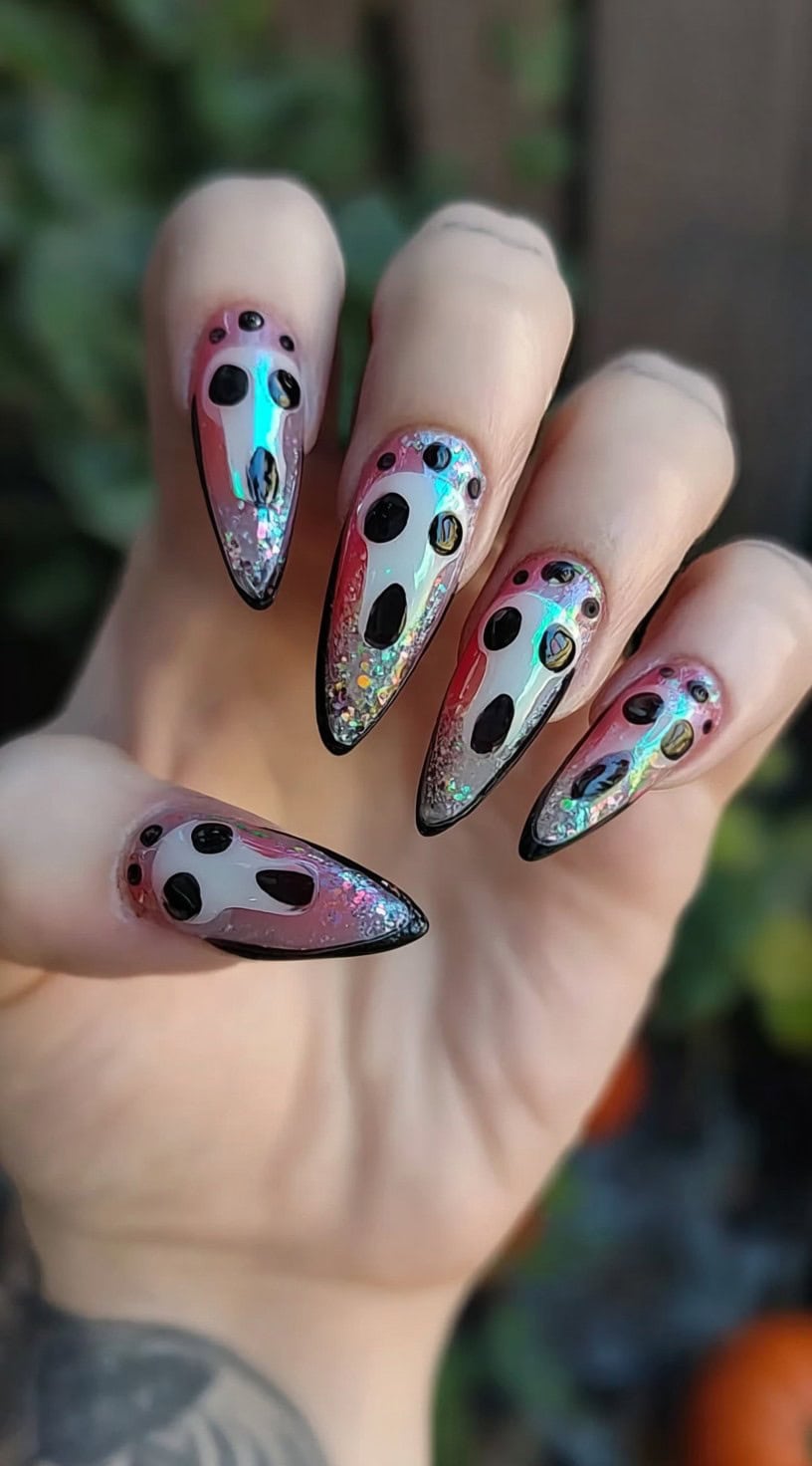 A hand with almond-shaped nails featuring holographic ghost faces on a glittery ombré base with black accents.