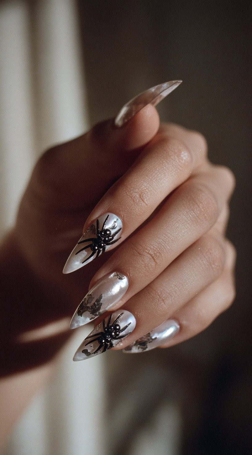A hand with metallic pearlescent nails and raised black 3D spider charms on two fingers.