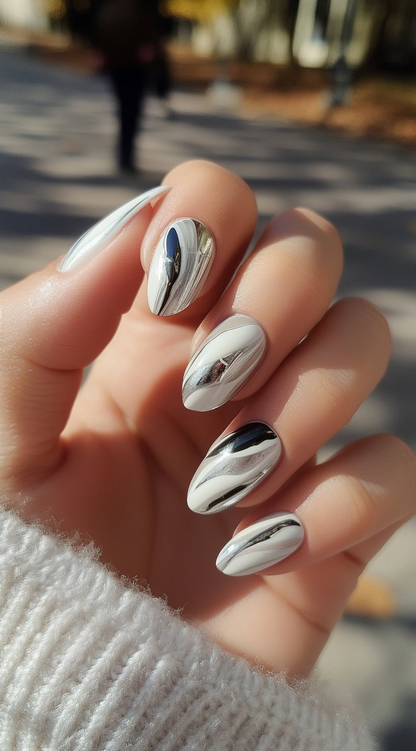 A close-up of a bride's hand with short almond nails featuring a mix of white polish and reflective silver chrome swirls for a bold, modern bridal look.