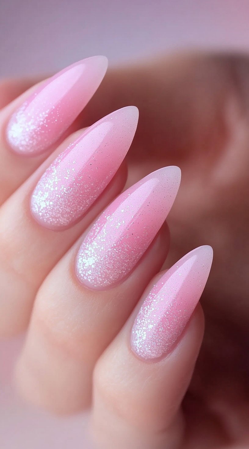Almond-shaped nails with a soft pink ombre design and a light dusting of fine white glitter.