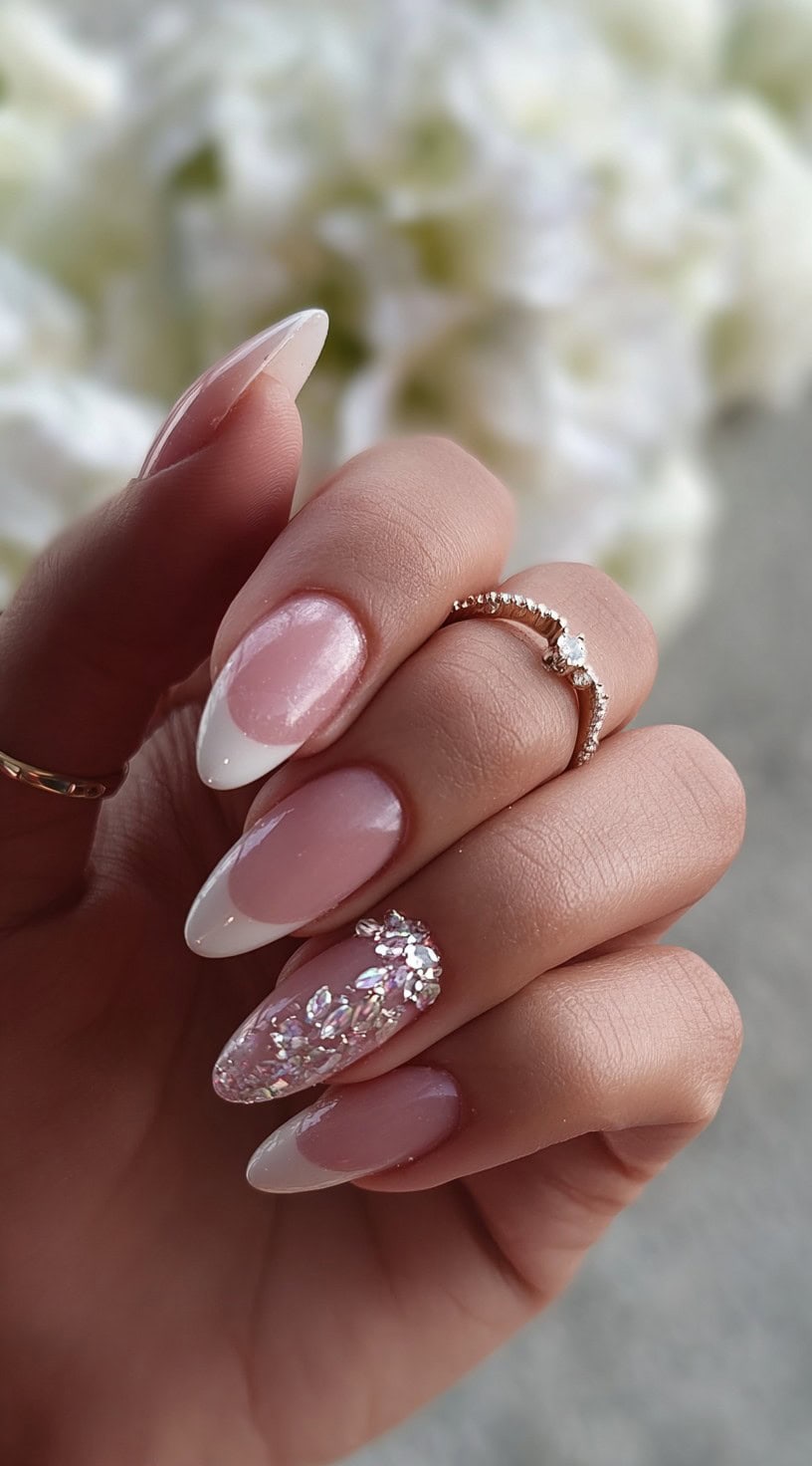 Almond-shaped nails with a glossy pink base and crisp white French tips, featuring one nail fully encrusted with iridescent crystals.