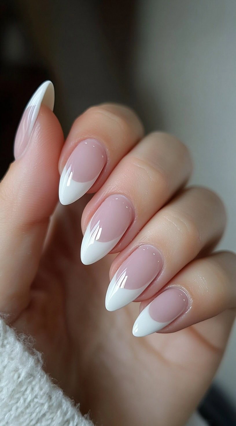 A hand with almond-shaped nails featuring a soft pink base and crisp white French tips, creating a timeless and elegant look.