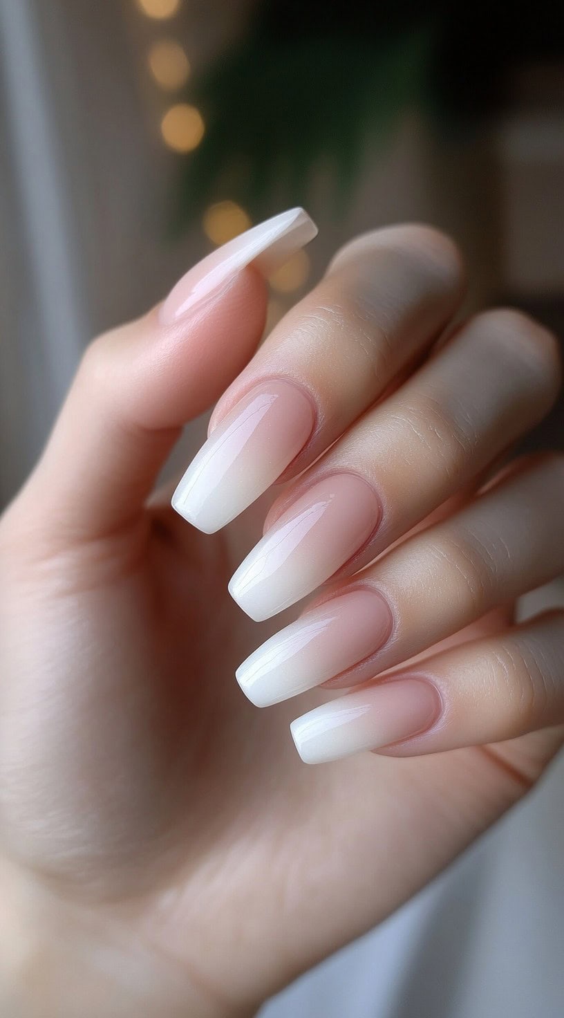 A hand with square-shaped nails featuring a seamless French ombre fade from nude to white with a glossy finish.
