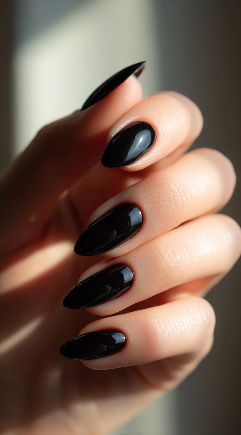 A hand with almond-shaped nails painted in a high-gloss black finish, catching natural light.