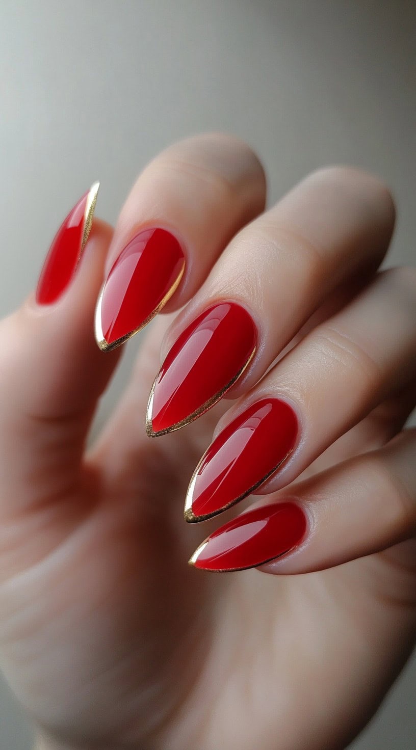 Elegant almond-shaped nails in a glossy red shade, topped with delicate gold French tips.