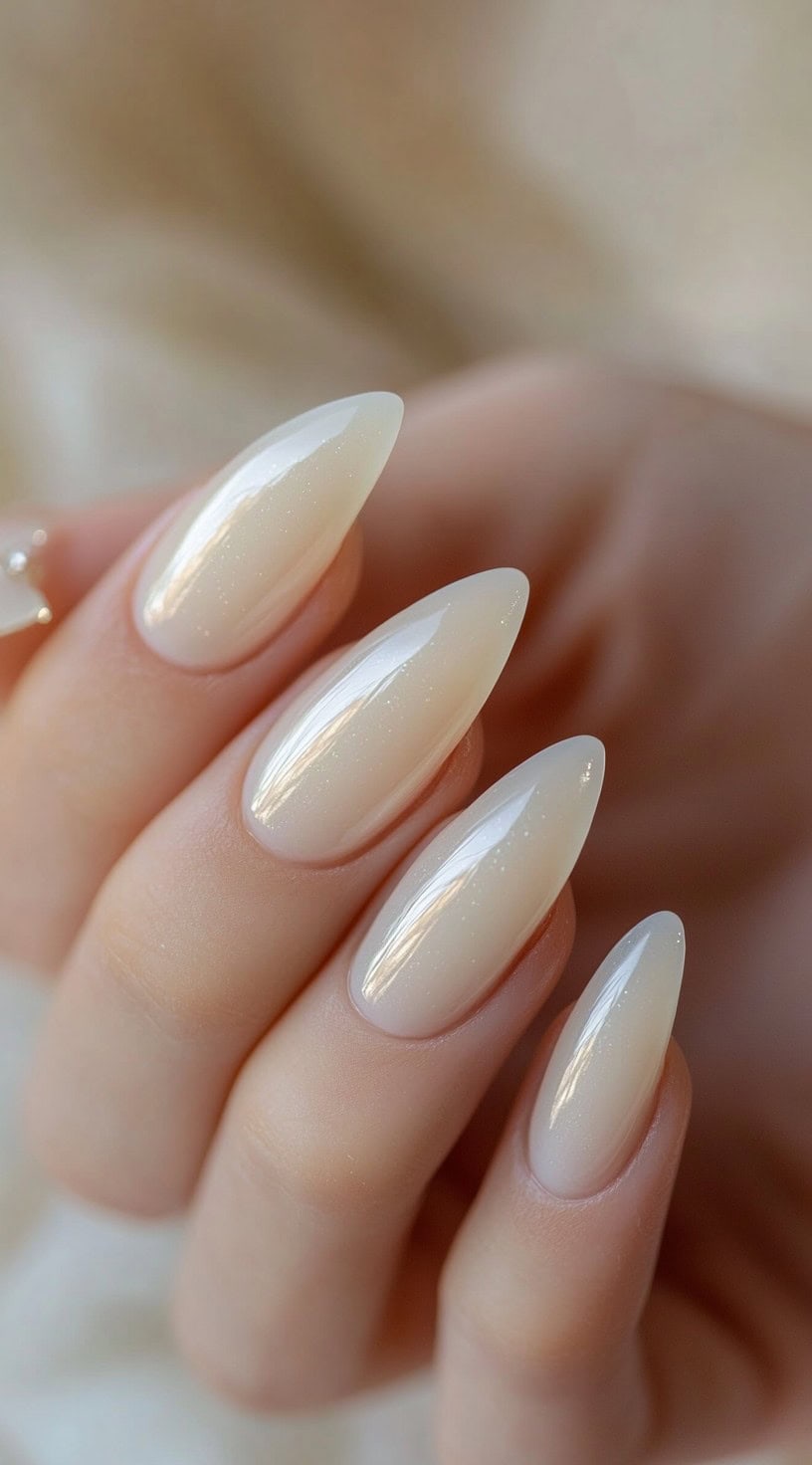 A close-up of almond-shaped nails coated in a soft milky-white polish with a glossy, pearl-like finish.