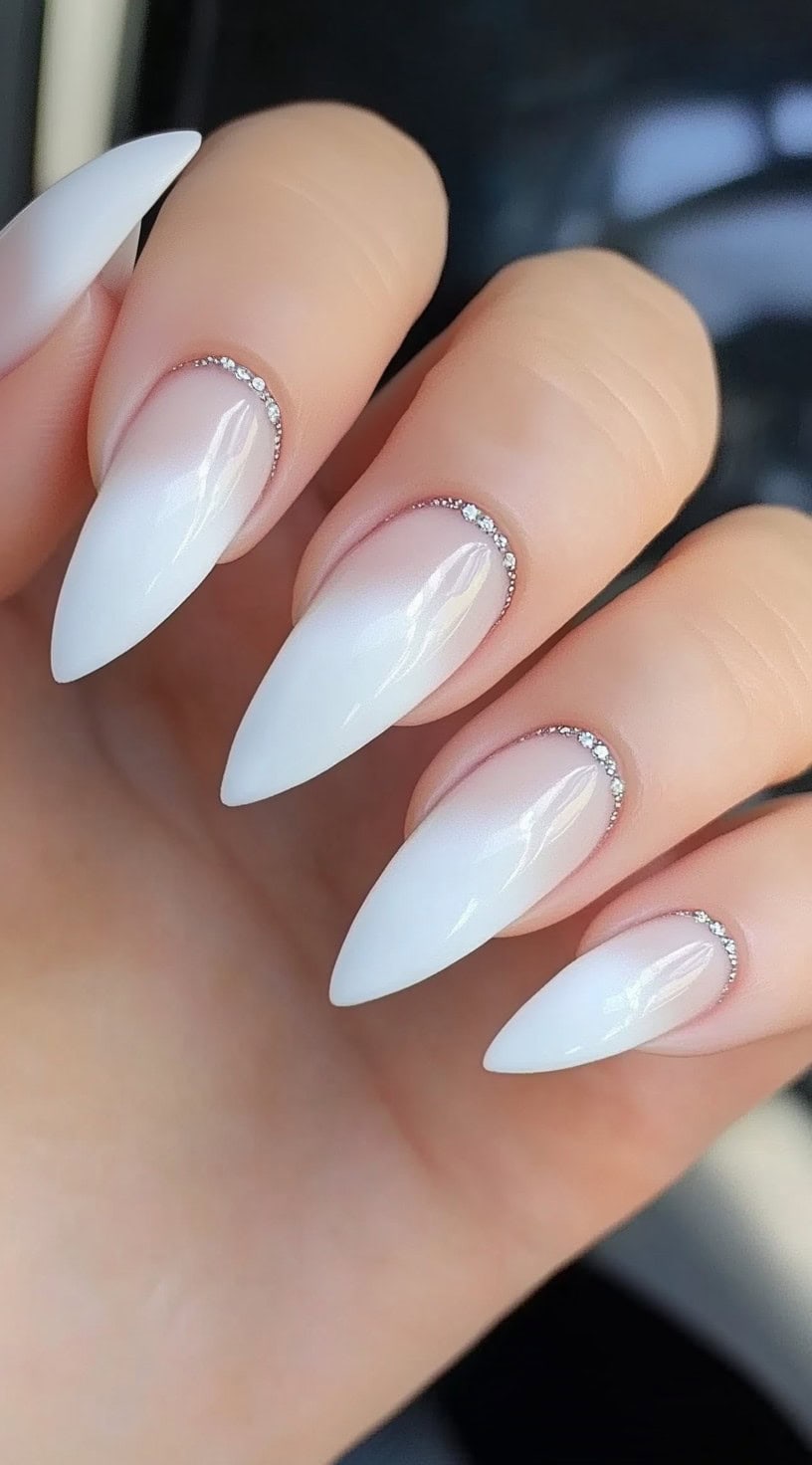 Elegant, almond-shaped nails with a subtle white ombre effect, finished with a fine line of tiny crystals near the cuticles.
