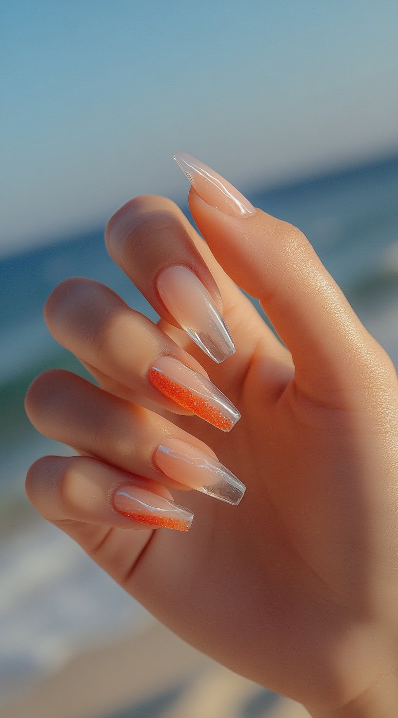 Long coffin nails with a clear, glossy base and coral glitter accents on two nails, creating a vibrant and airy look.