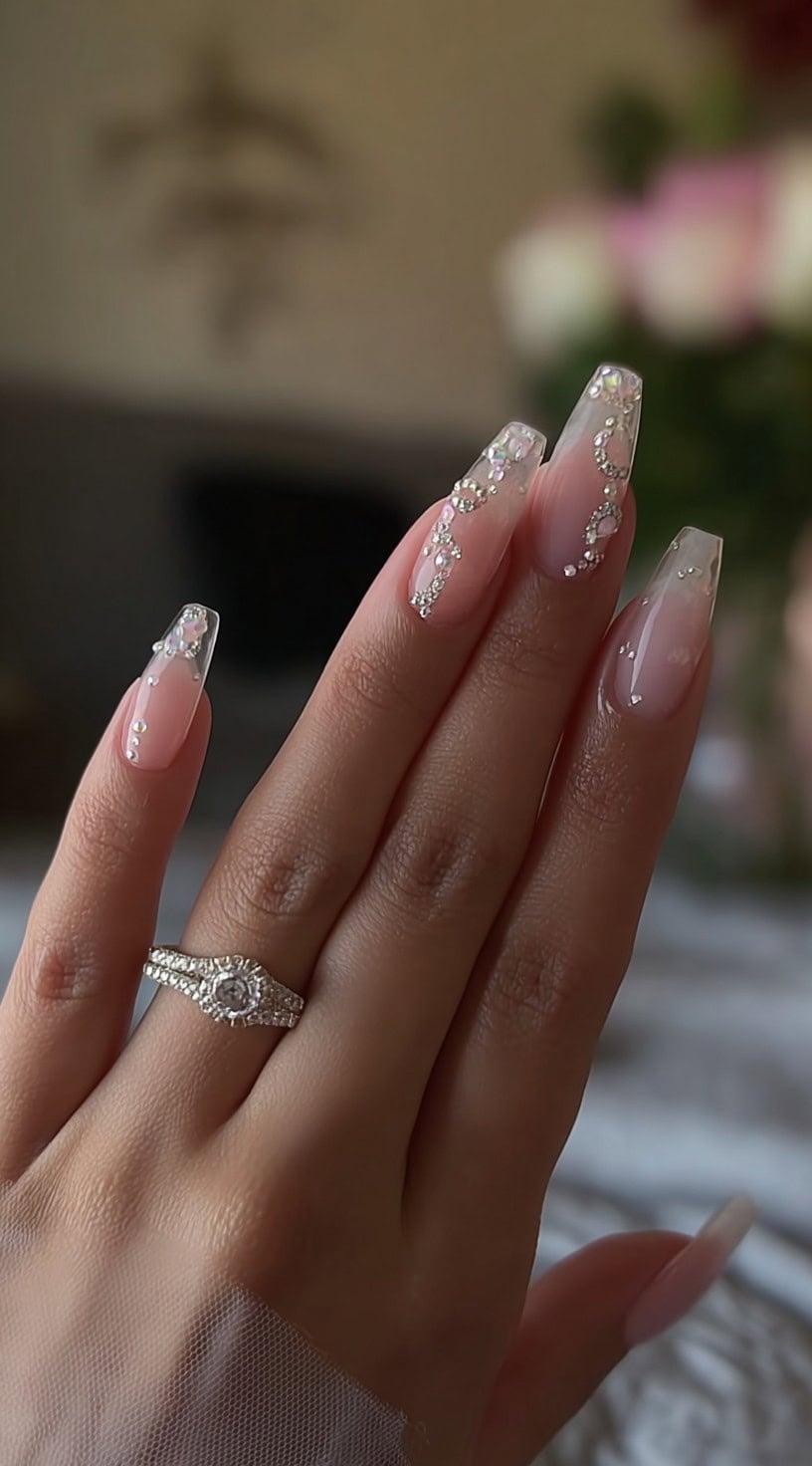 Long clear coffin nails with a soft nude fade and swirling rhinestone arrangements forming delicate, floating chain-like patterns.